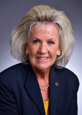 Karen Lackey smiling in a yellow top and navy blue coat