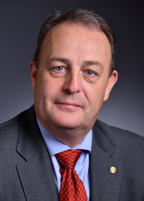 Mark Minton posing in a grey suit with a red tie